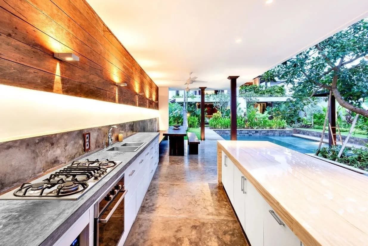 Modern kitchen with long counter, concrete wall, and outdoor view of pool.