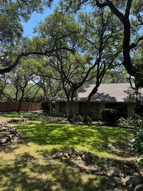 A house with a brown roof surrounded by trees and a grassy yard on a sunny day.