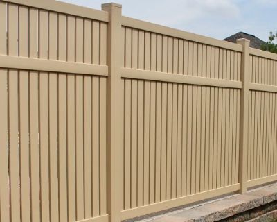 A tan wooden fence is sitting next to a stone wall.