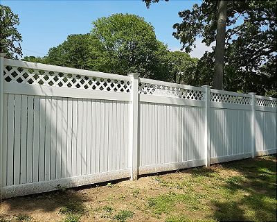A white fence with a lattice design is surrounded by grass and trees.