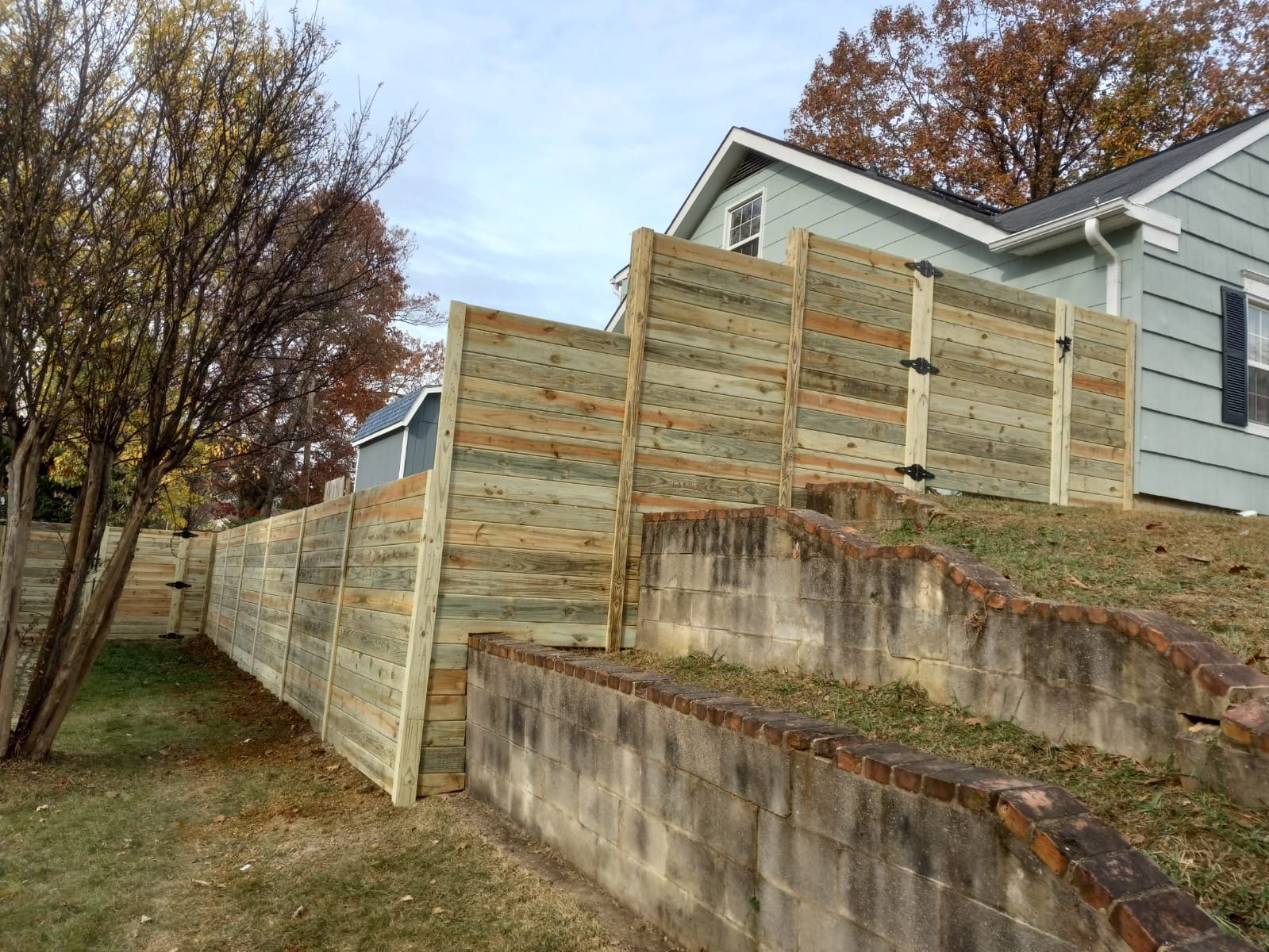 A wooden fence surrounds a brick wall in front of a house.