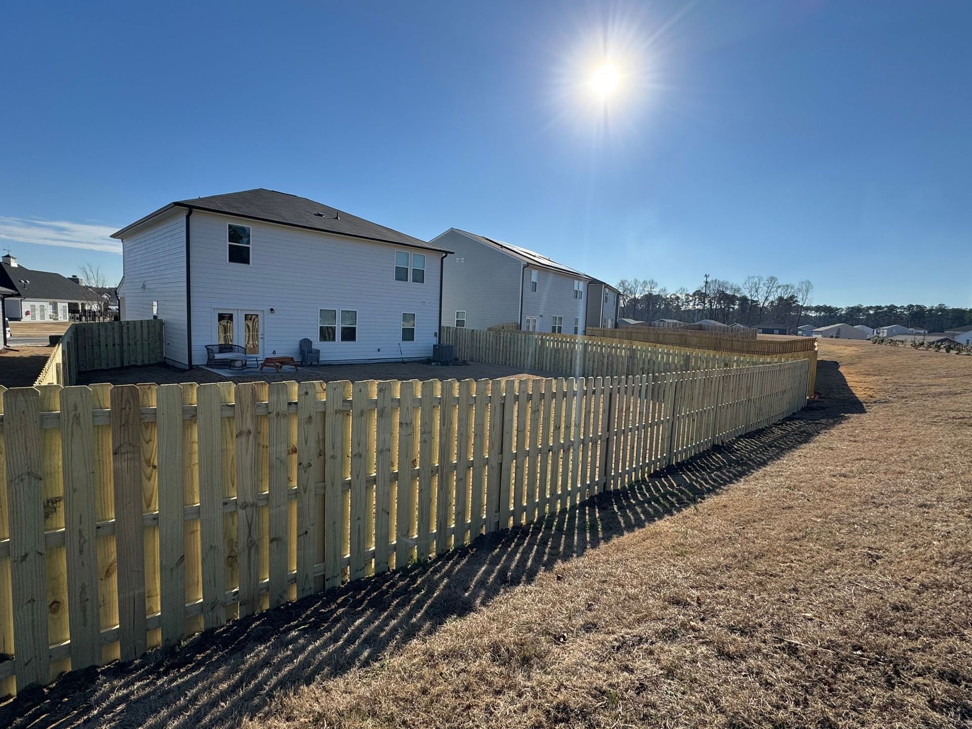 A wooden fence surrounds a large field in front of a house.