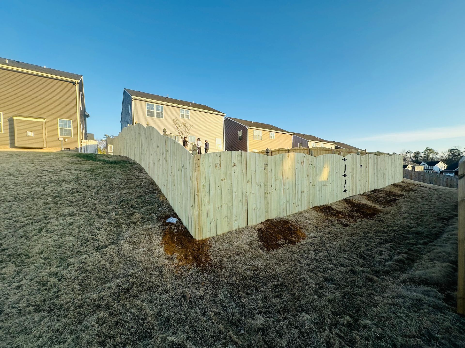 A wooden fence is sitting on top of a grassy hill in front of a house.
