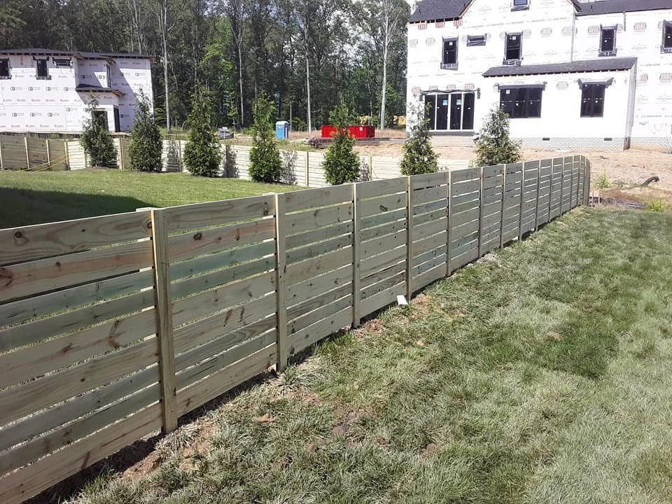 A wooden fence surrounds a lush green yard in front of a house under construction.