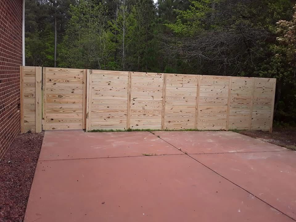 A wooden fence surrounds a concrete driveway in front of a brick building.