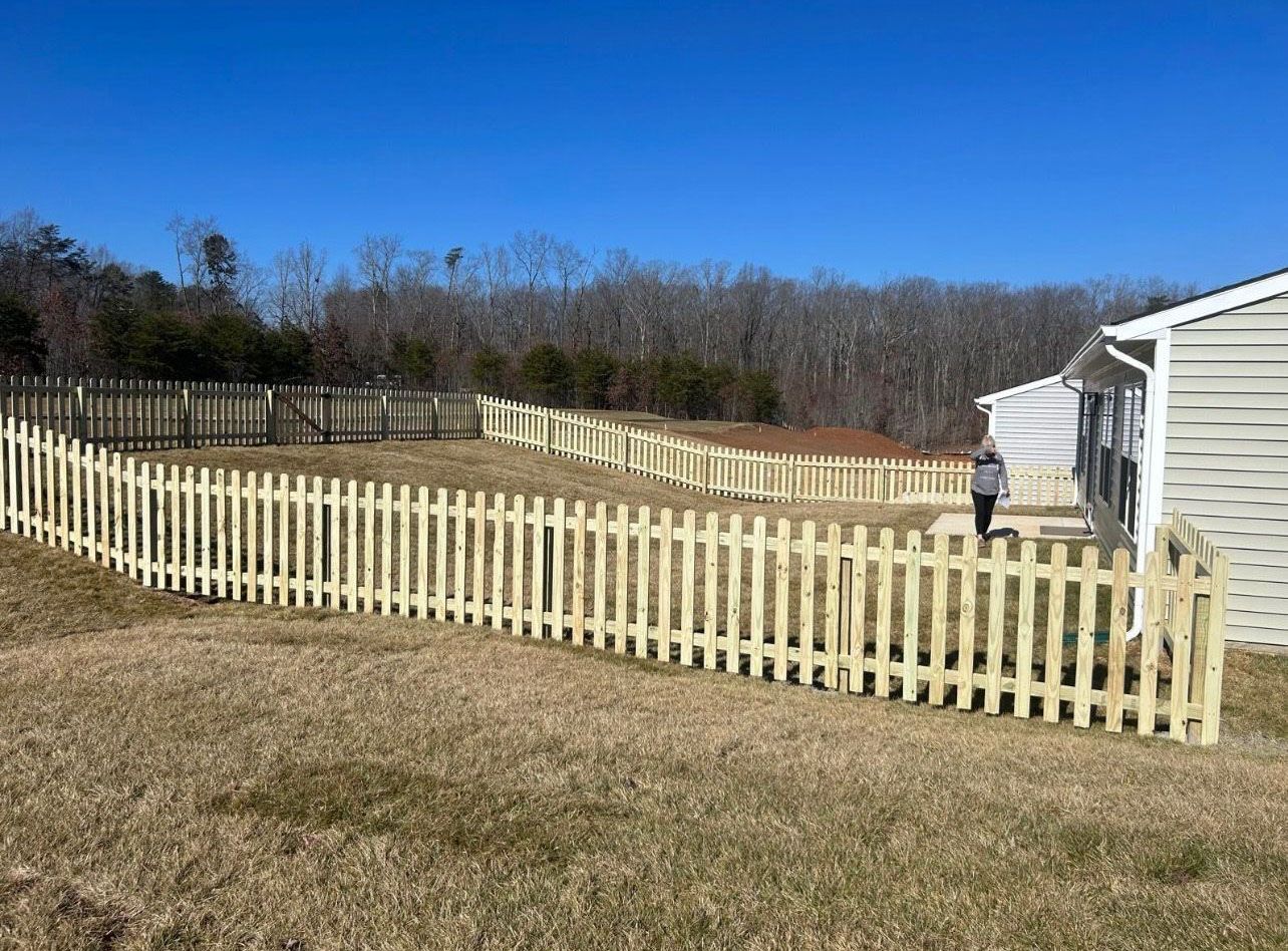A wooden picket fence is surrounding a house in a field.
