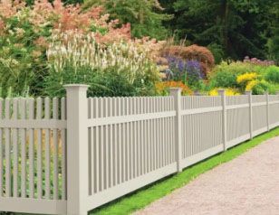 A white picket fence surrounds a garden with flowers.