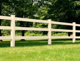 A white fence surrounds a grassy field with trees in the background.