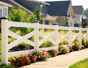 A white fence is surrounded by flowers and houses in a residential area.