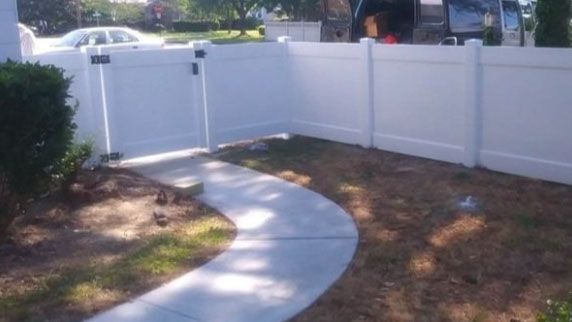 A white fence with a concrete walkway leading to it.