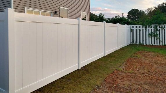 A white vinyl fence is in the backyard of a house.