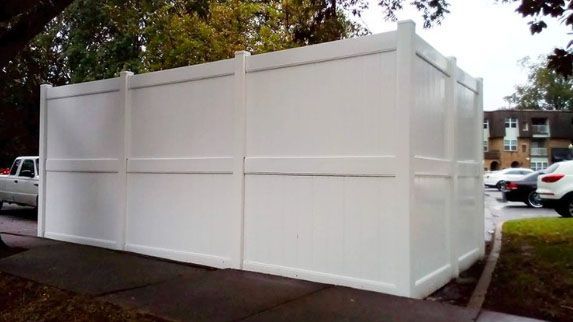 A white fence is sitting on the sidewalk next to a parking lot.