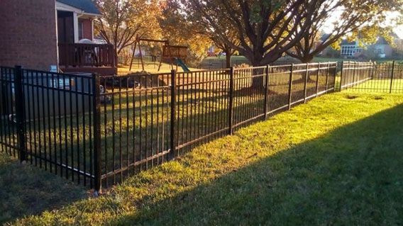 A black fence surrounds a lush green yard in front of a house.