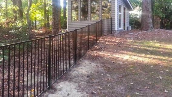 A black wrought iron fence surrounds a small house in the woods.