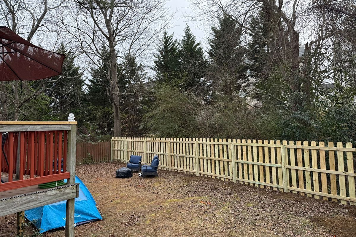 A wooden fence surrounds a backyard with a deck and chairs.