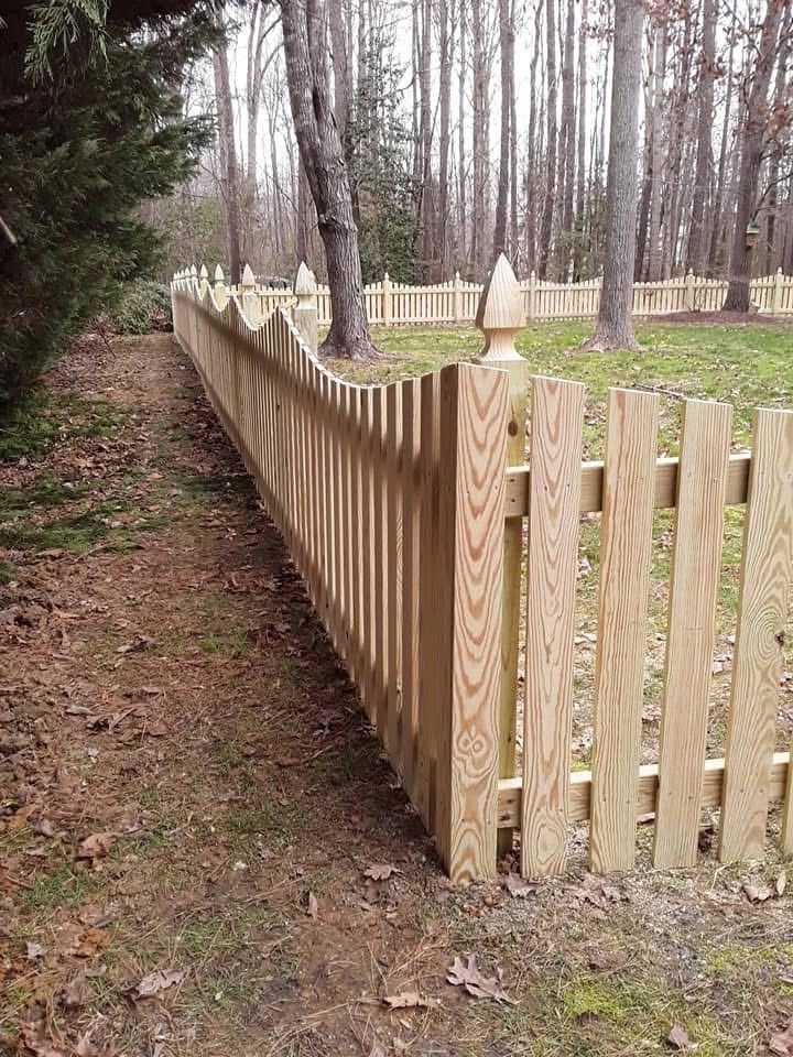 A wooden picket fence surrounds a yard in the woods.