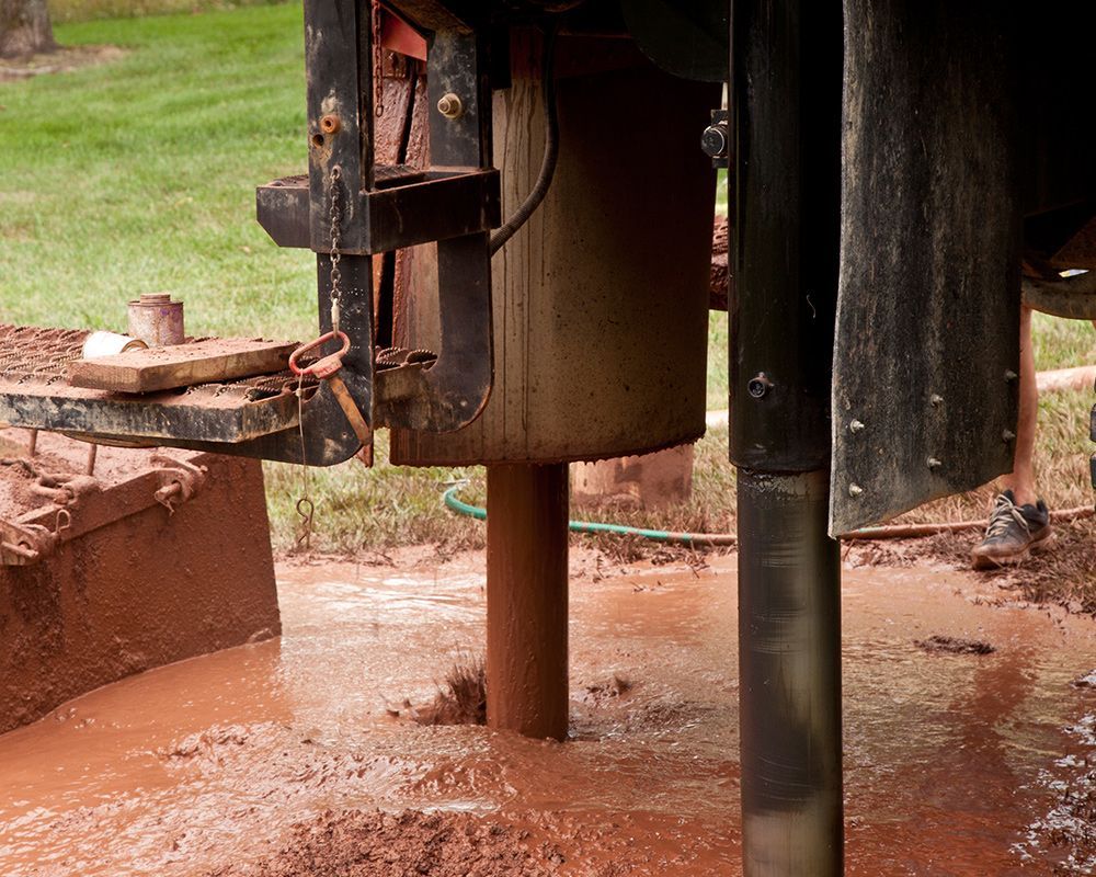 Drilling rig, drilling into muddy ground, ejecting brown fluid. Outdoors, close-up shot.