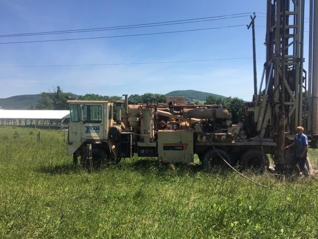 Drilling rig on a truck in a grassy field; a person operates the machinery.