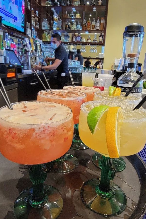 A tray of margaritas with straws on a table in a restaurant.
