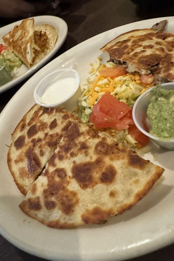 A white plate topped with quesadillas guacamole and sour cream