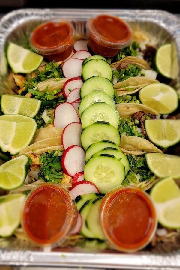 A tray of food with tacos , cucumbers , radishes , limes and sauces.