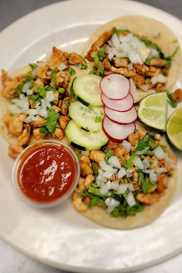 A close up of a plate of tacos with sauce and vegetables on a table.