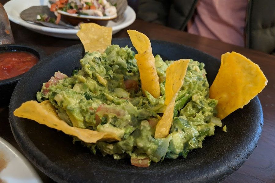 A bowl of guacamole with tortilla chips on a table.