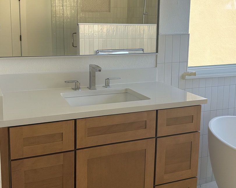 Bathroom with light wood cabinets, white countertop, rectangular sink, and rectangular tiles.