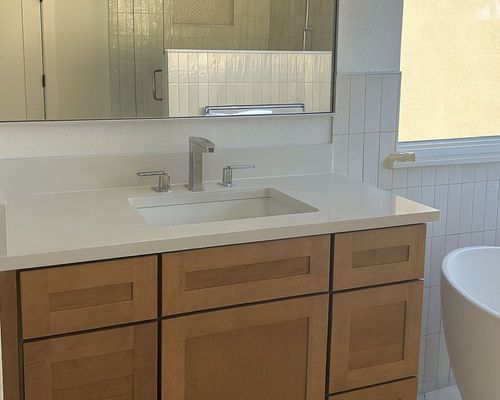 Bathroom with light wood cabinets, white countertop, rectangular sink, and rectangular tiles.