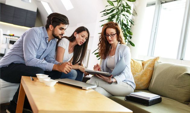 Three people reviewing a tablet on a couch in a bright living room