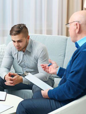 Two men in a counseling session, one taking notes while the other speaks on a couch.