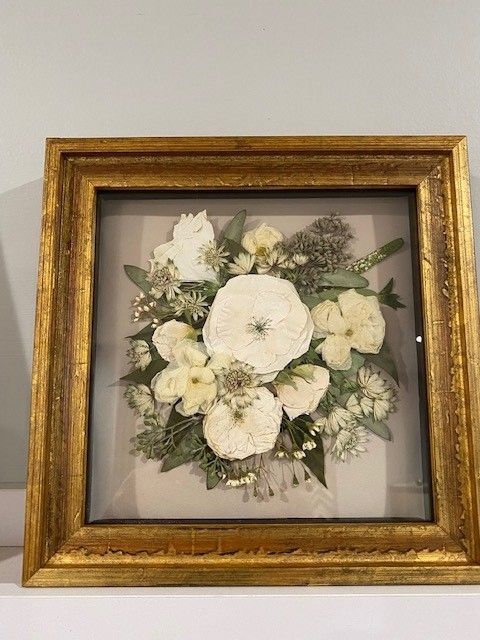 A picture of a bouquet of white flowers in a gold frame.
