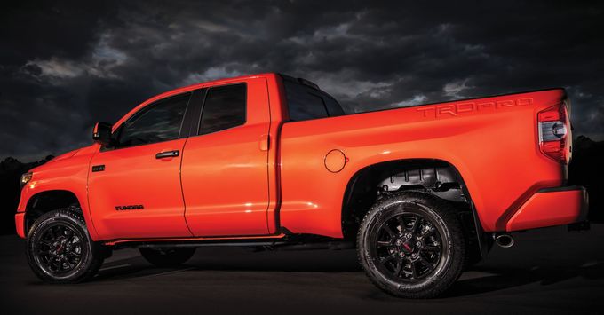 Bright red pickup truck in a dark studio setting, side view with black wheels