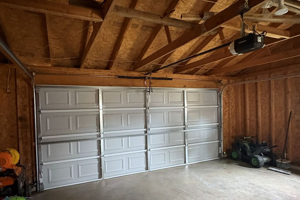 Garage interior with a partially open white garage door. A lawnmower and tools are visible.
