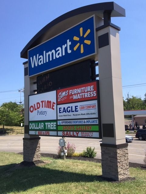 Sign for a shopping center, with Walmart logo at the top, followed by other businesses and names.