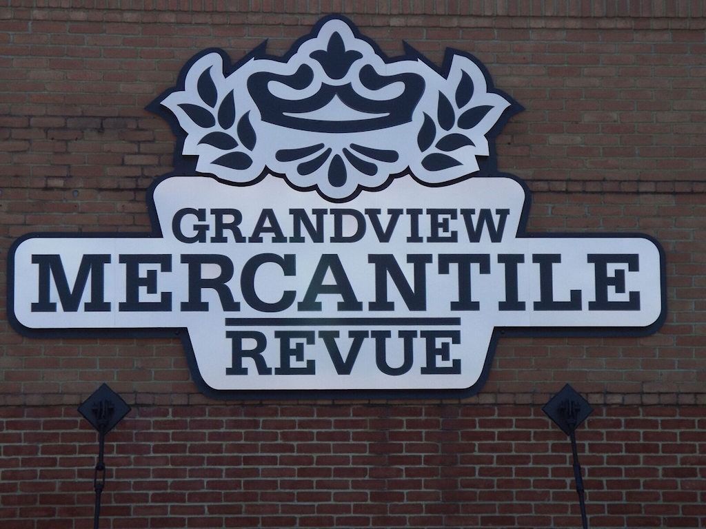 Sign for Grandview Mercantile Revue: silver lettering on brick building, with crown and leaf design.