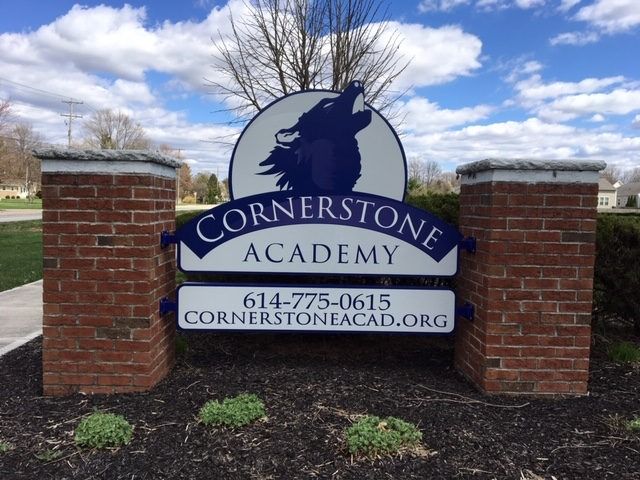 Sign for Cornerstone Academy: brick pillars, blue and white sign with wolf logo, contact info, and website.