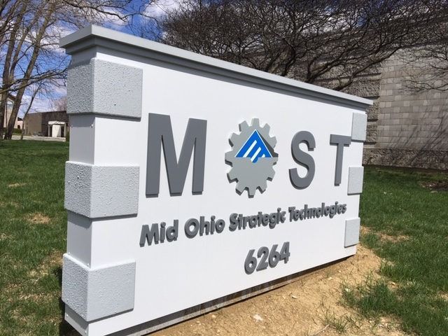 Sign for Mid Ohio Strategic Technologies, gray and white with building, grass, and trees in the background.