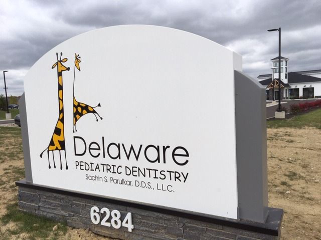 Sign for Delaware Pediatric Dentistry with giraffe logo, near a building, 6284.