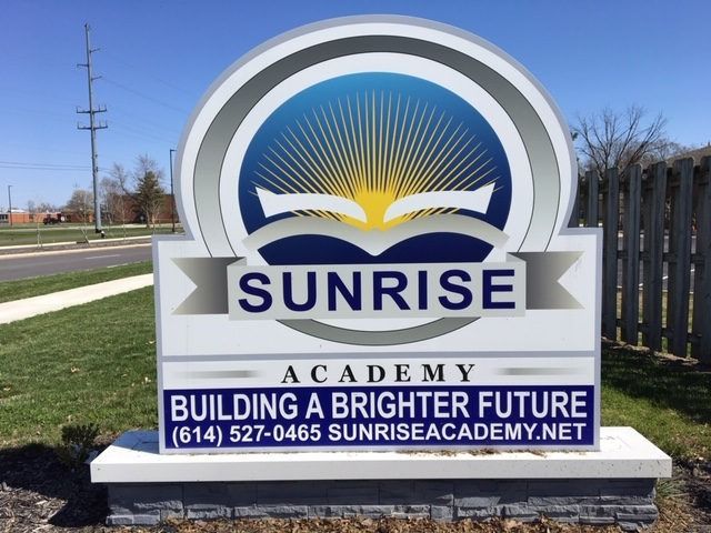 Sunrise Academy sign with logo over a blue, green, and white background; 