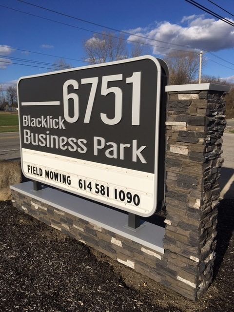 Sign for Blacklick Business Park, with address 6751, stone and concrete base, on a sunny day.