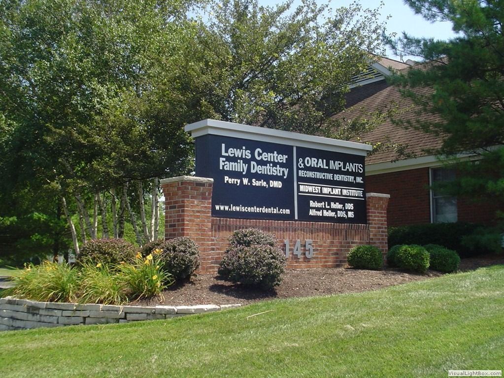 Sign for Louis Center Family Dentistry and Oral Implants at 149, with a brick base and greenery.