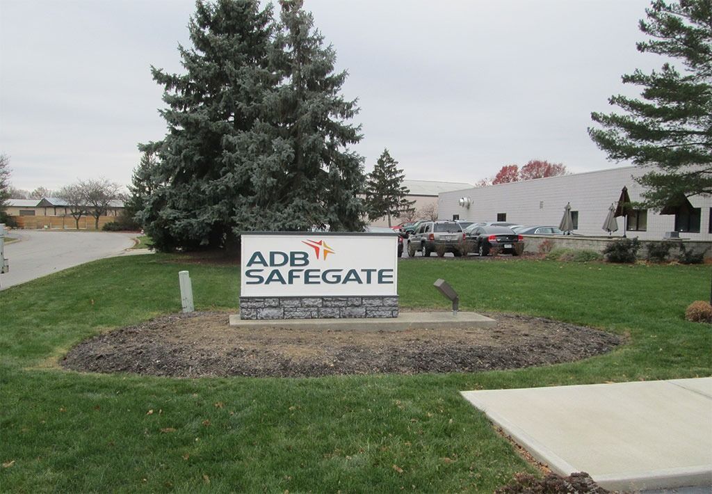 ADB SAFEGATE sign in front of a building with a grassy area and trees on a cloudy day.