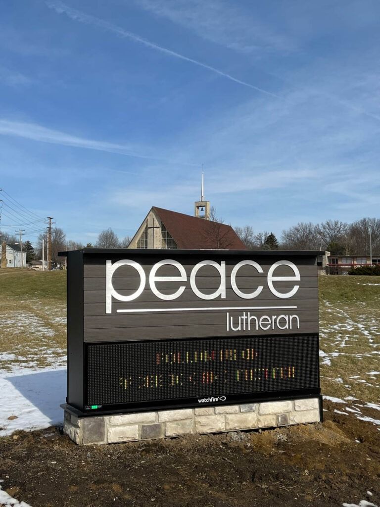 Sign for Peace Lutheran Church with the church building in the background under a blue sky.