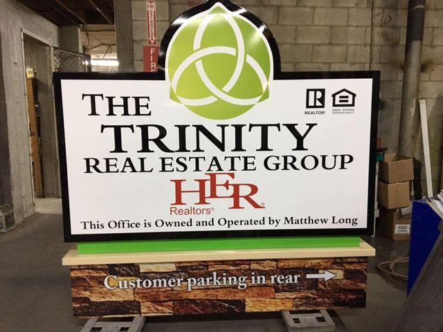 Sign for The Trinity Real Estate Group. Features logo, text, and 