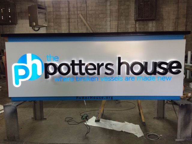 Illuminated sign for The Potter's House, with a blue and white logo, black text, and the phrase 