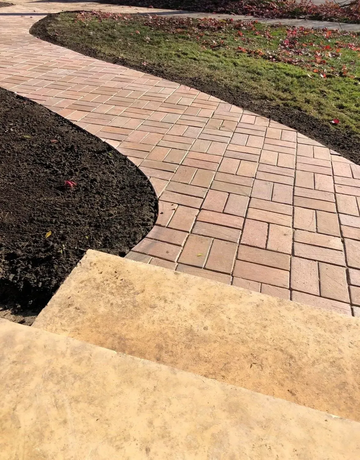 Brick pathway curving through mulch and grass, leading from a concrete step.
