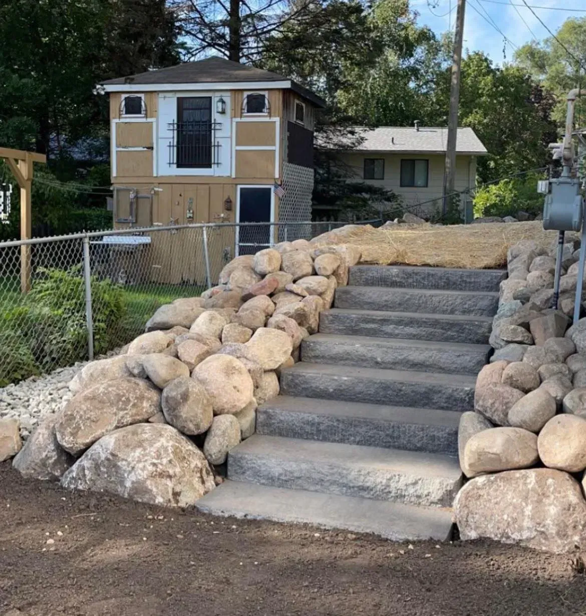 Stone steps leading up to a small building with a fence and a house in the background.