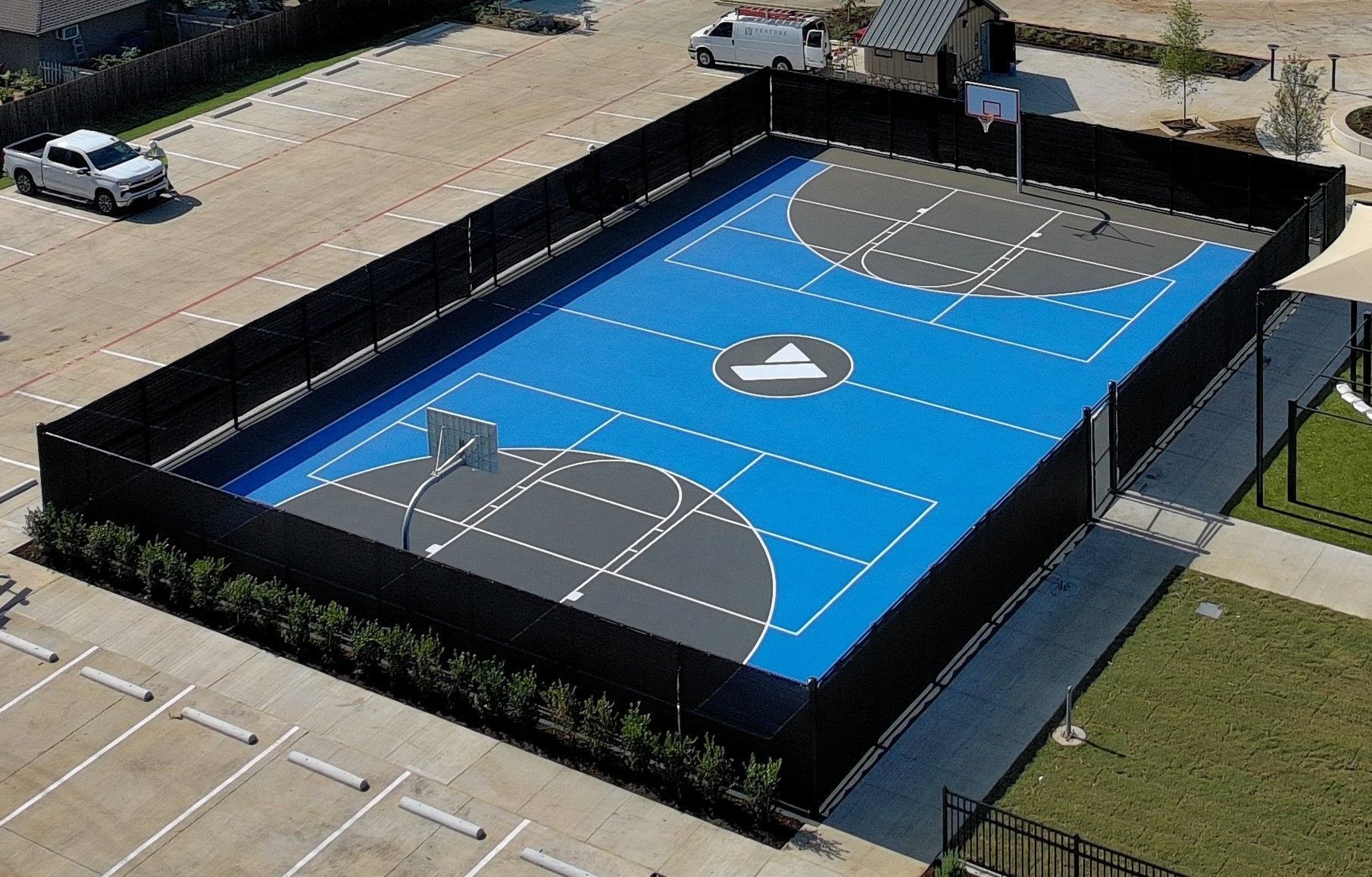 Aerial view of an outdoor blue basketball court with black fencing and painted lines