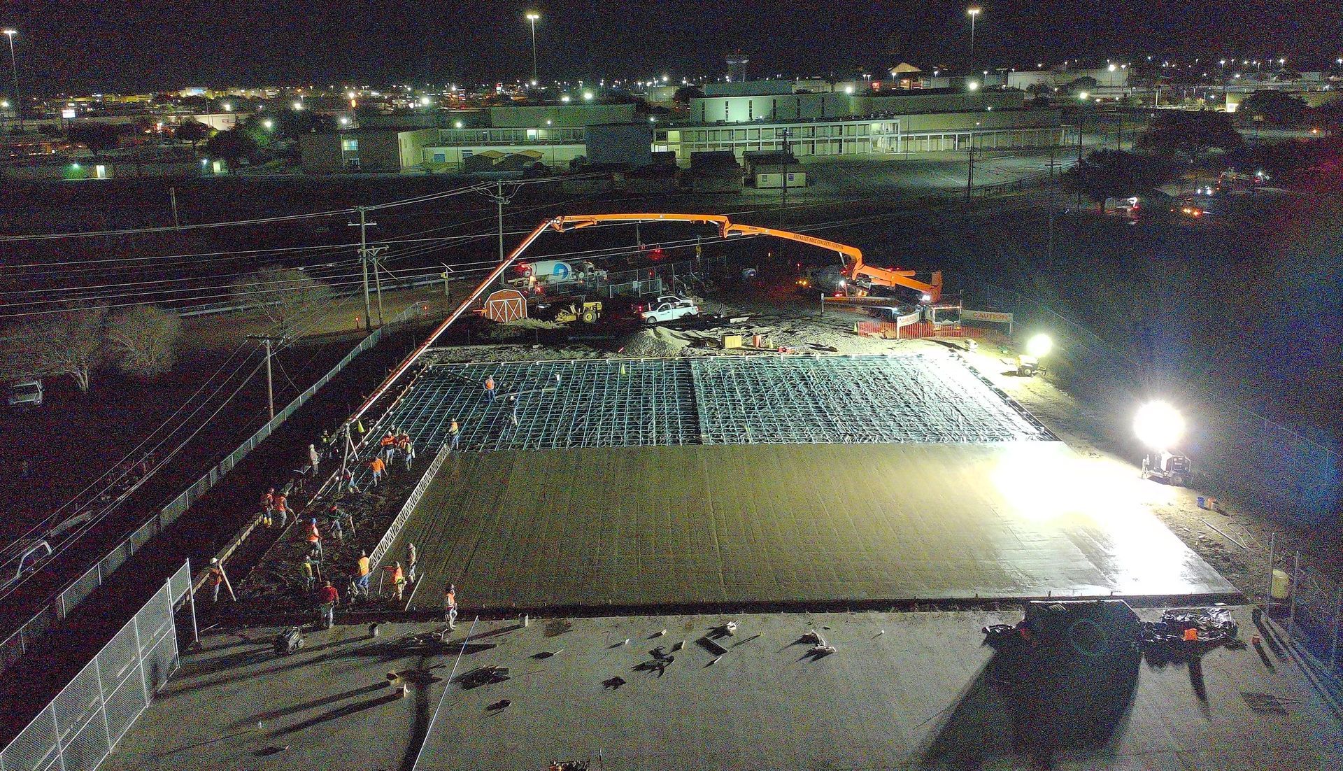 Construction workers pouring concrete at night, large flat surface lit by spotlights, industrial background.